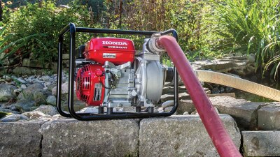 Wide view of transfer pump sitting on stones with hose plugged in. 