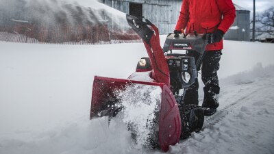 Wide view of a person clearing a path with a snowblower in front of a big barn.
