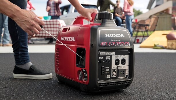 A person is using a Honda generator as it sits outside on the pavement.