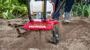 Head-on view of gardener pushing tiller through very dry and dusty soil.  